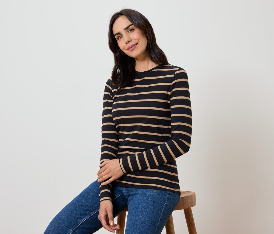 Žena sedí na stoličce v černém tričku s béžovými pruhy a modrých džínách.