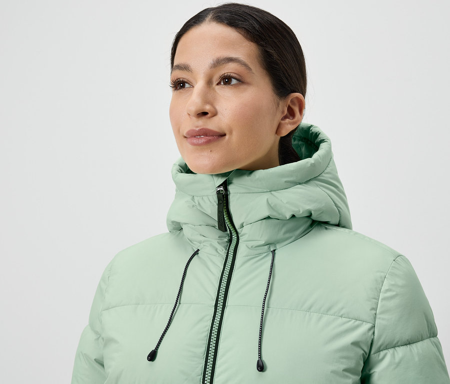 Žena má na sobě světle zelenou péřovou bundu.