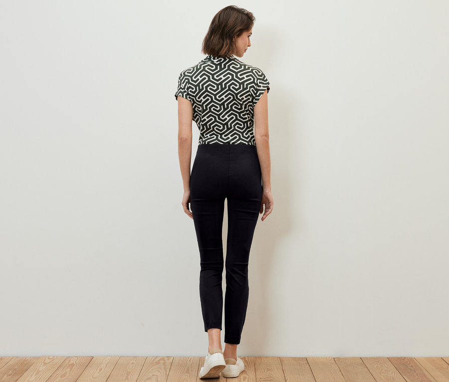 Žena stojí zády k fotoaparátu a má na sobě černé strečové kalhoty.