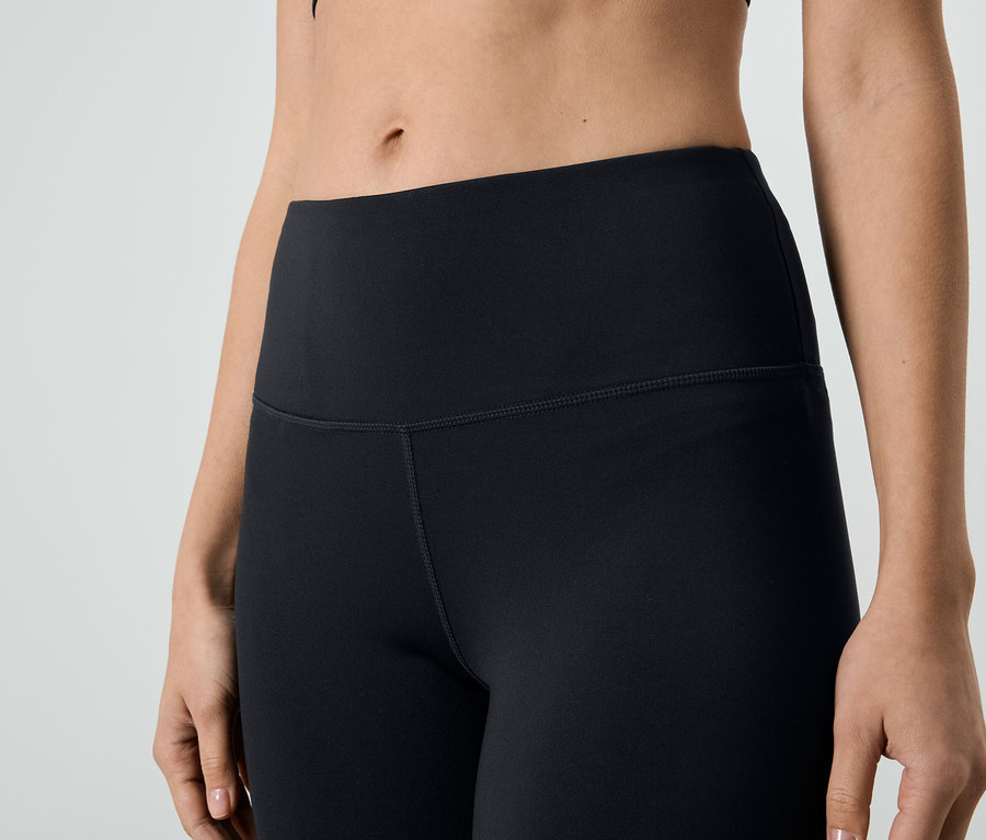 Detailní záběr ženy v černých legínách a sportovním topu.