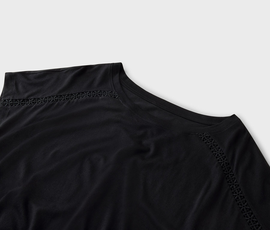 Detailní záběr na černý top s dírkovanou výšivkou podél výstřihu.