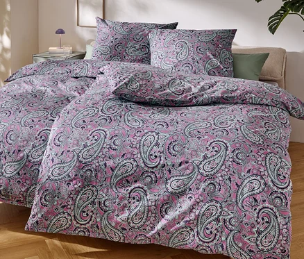 Detailní záběr na postel s růžovým ložním prádlem s paisley vzorem.