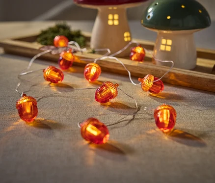 Detailní záběr světel ve tvaru žaludů na stole vedle houbových lamp na dřevěném podnosu.