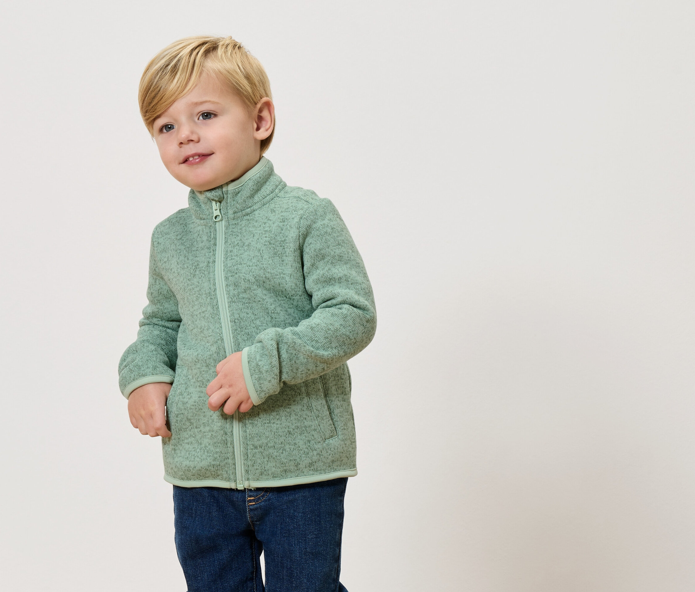 Blonďatý chlapec má na sobě světle zelenou fleecovou bundu a džíny.