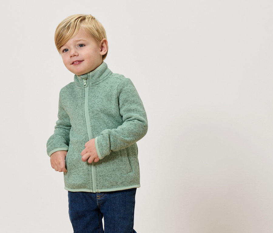 Blonďatý chlapec má na sobě světle zelenou fleecovou bundu a džíny.