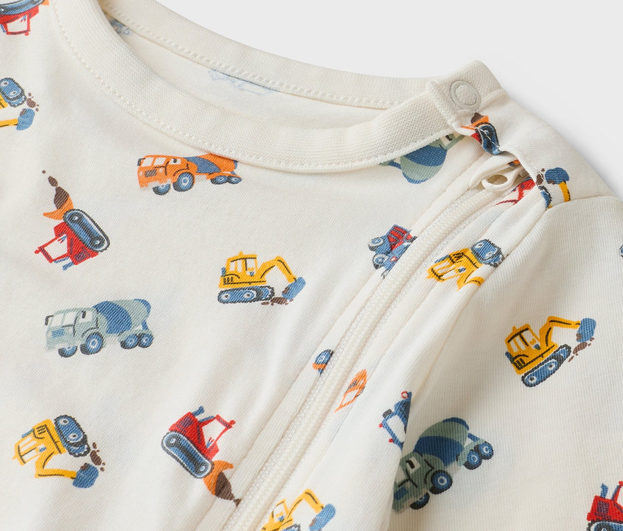 Detailní záběr krémového dětského overalu na zip se vzorem stavebních vozů.
