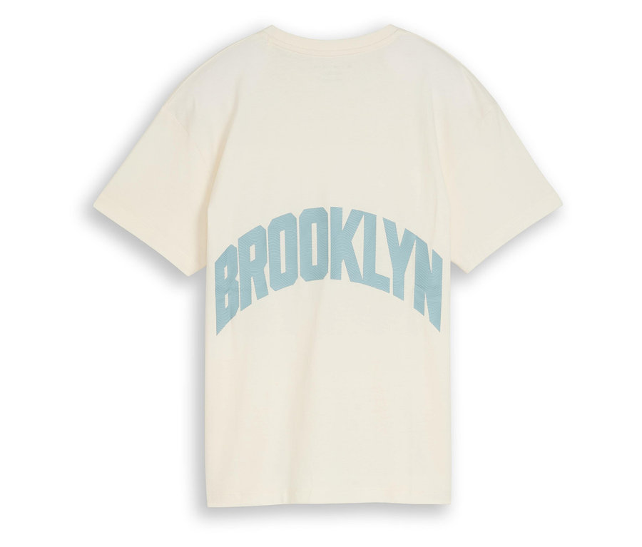 Detailní záběr na krémové tričko s modrým nápisem „Brooklyn“ na zadní straně.