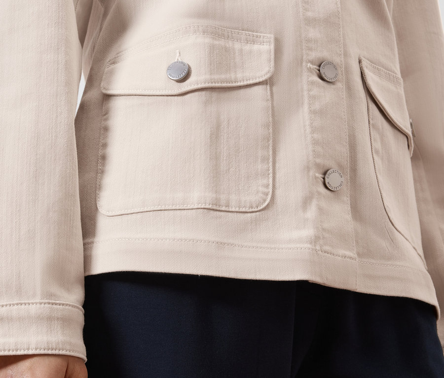 Detailní záběr na světle hnědou džínovou bundu se stříbrnými knoflíky a našitými kapsami.