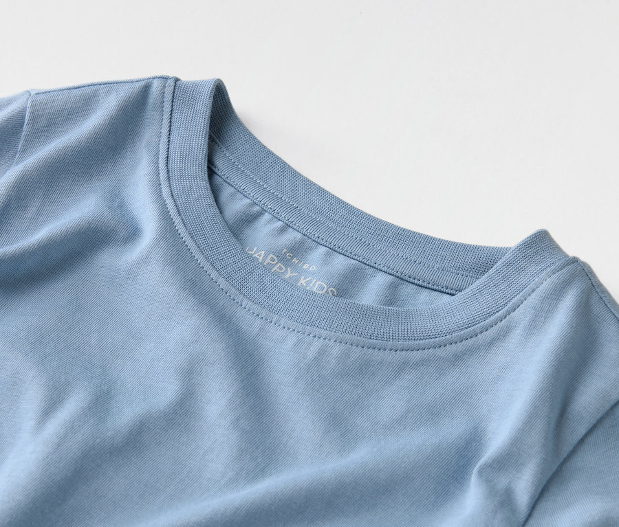 Detailní záběr světle modrého trička s nápisem "JAPPY KIDS" na límci.