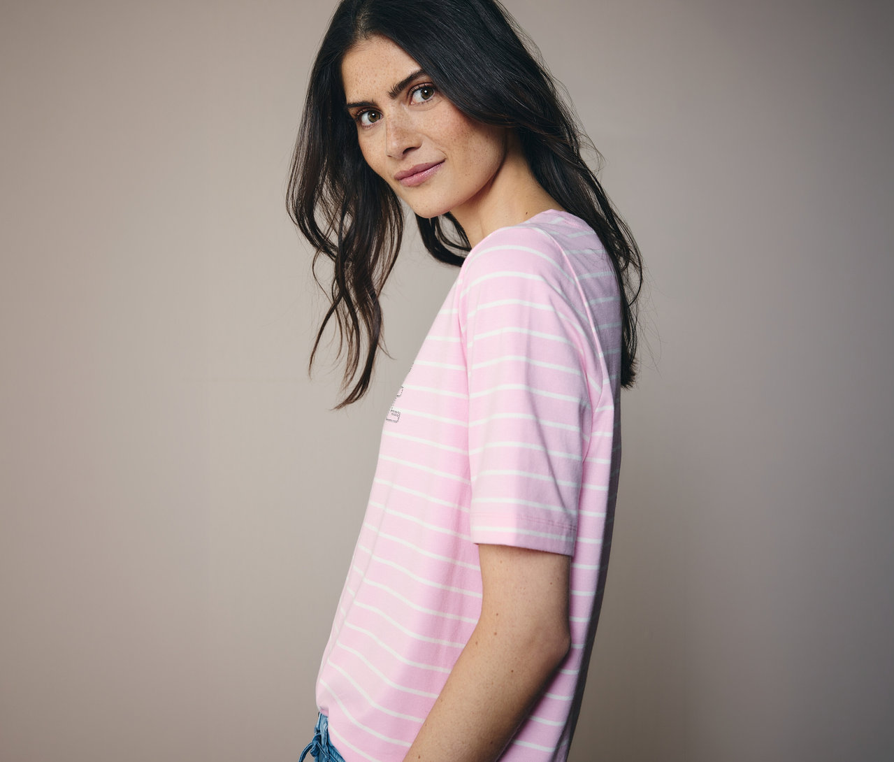 Žena se dívá přes rameno a má na sobě růžovo-bílé pruhované tričko CECIL.