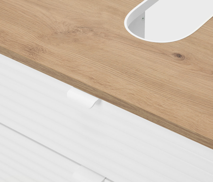 Detailní záběr na světlě hnědou dřevěnou desku s bílým oválným výřezem a bílými zásuvkami pod ní.