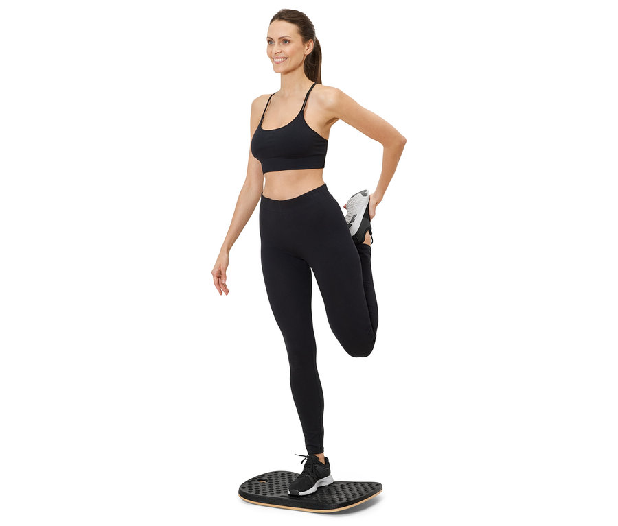 Žena protahuje nohu na balanční desce, má na sobě sportovní oblečení.