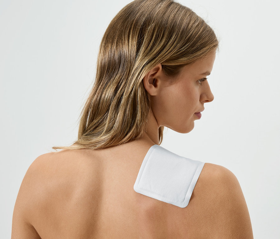 Žena s bílou hřejivou náplastí na rameni, dívá se doprava.