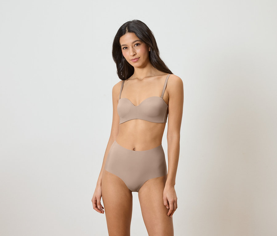 Žena má na sobě béžovou podprsenku bez ramínek a kalhotky s vysokým pasem.