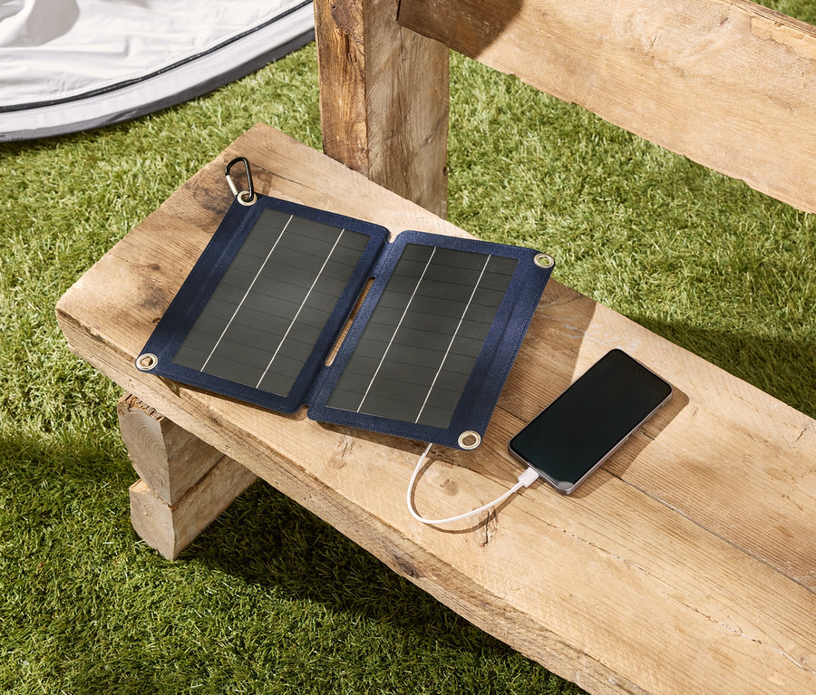 Solární panel nabíjí smartphone ležící na dřevěné lavičce venku.