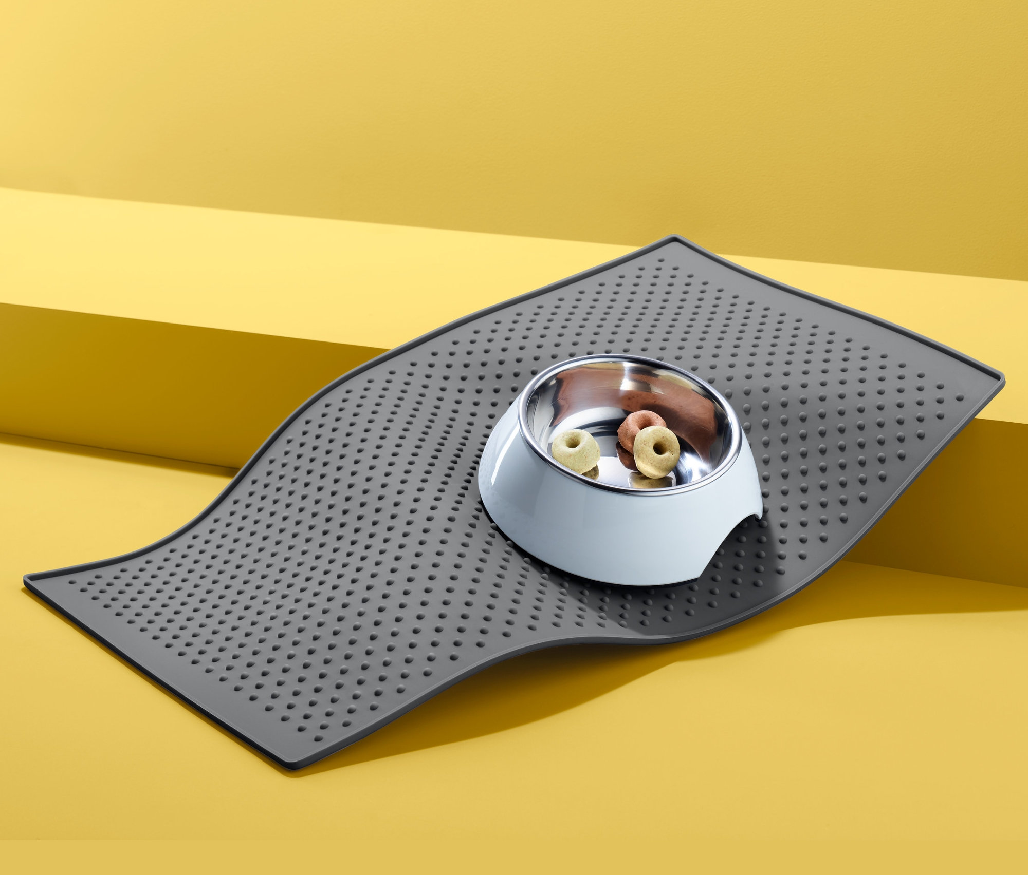 Šedá podložka pod misku na krmivo s miskou pro zvířata plnou krmiva na žlutém pozadí.