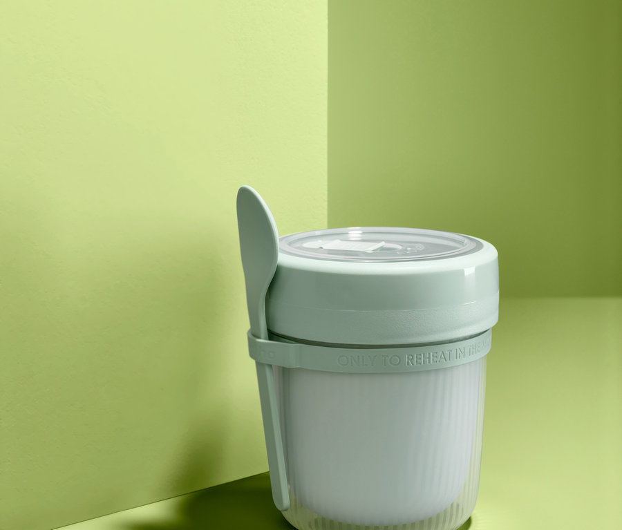 Cestovní hrnek na polévku s lžící na zeleném pozadí.