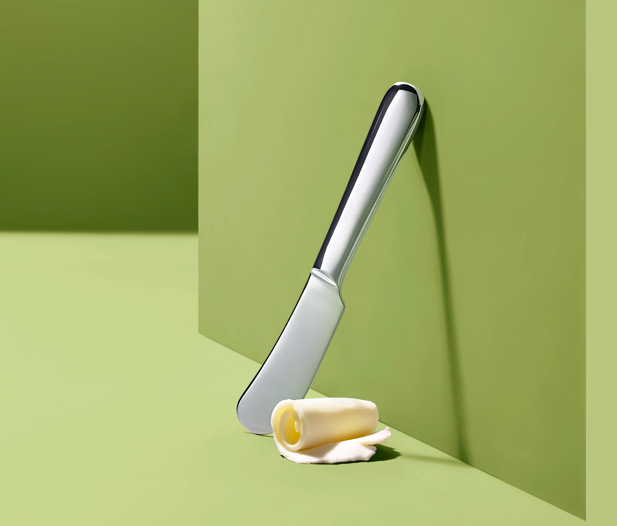 Nůž na máslo a rolka másla na zeleném pozadí.