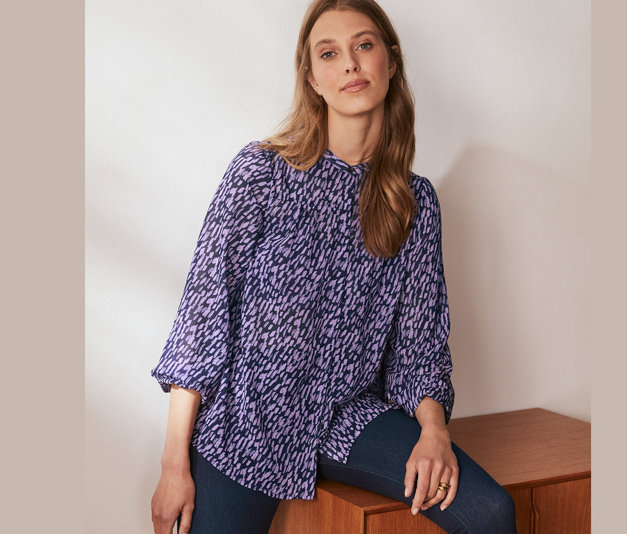 Žena sedí na skříňce a má na sobě halenku s potiskem.