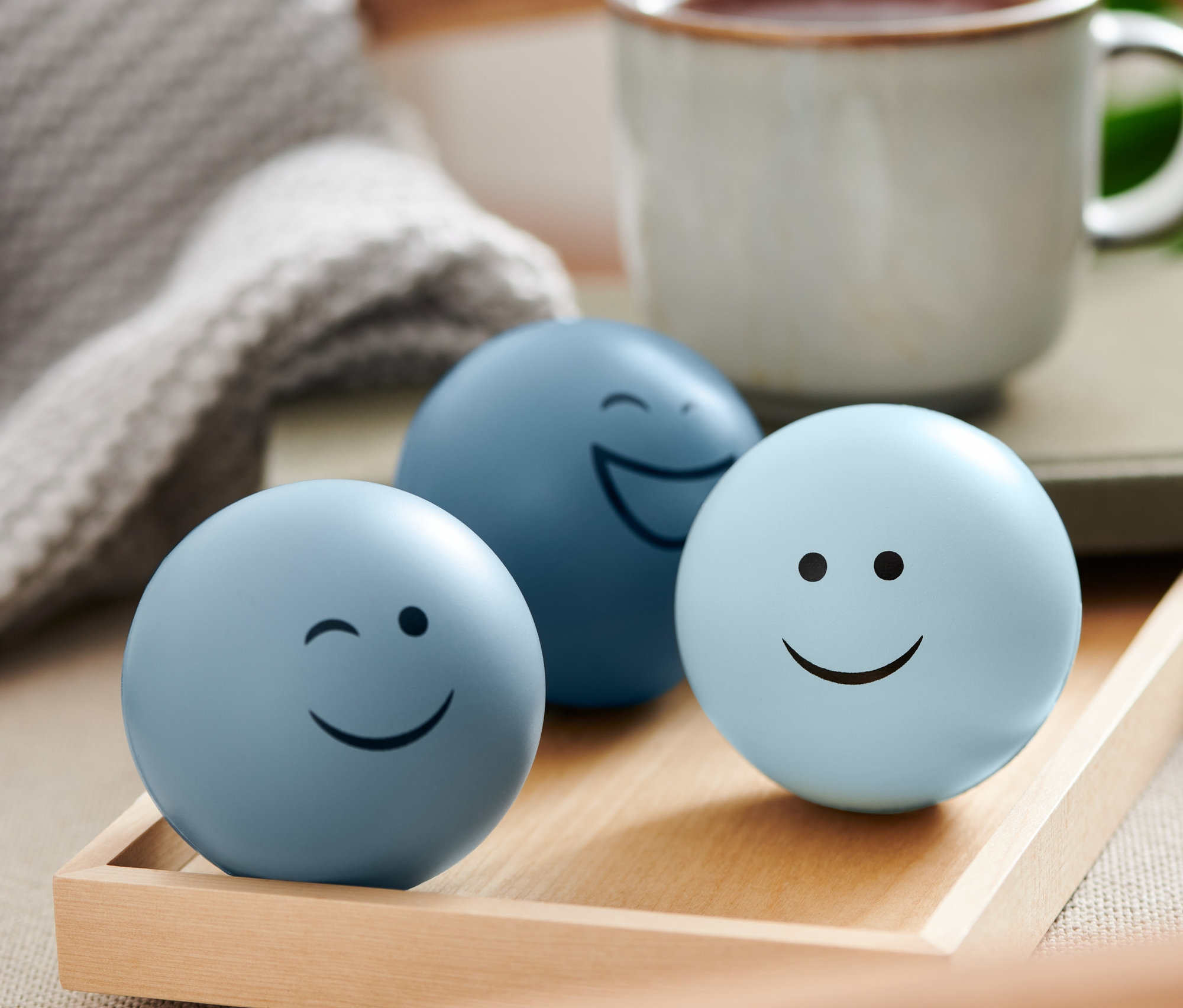 Tři antistresové míčky s obličeji na dřevěném podnosu.