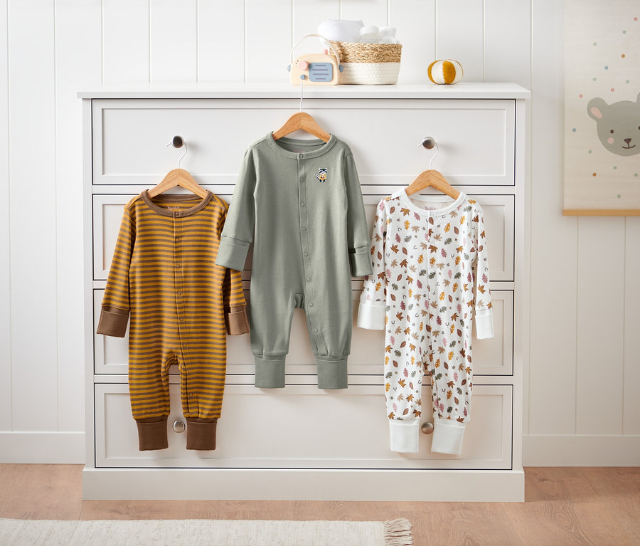 Tři pyžamka visí na komodě.