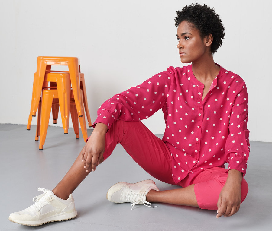 Žena sedí na podlaze a má na sobě puntíkovanou tkanou halenku.