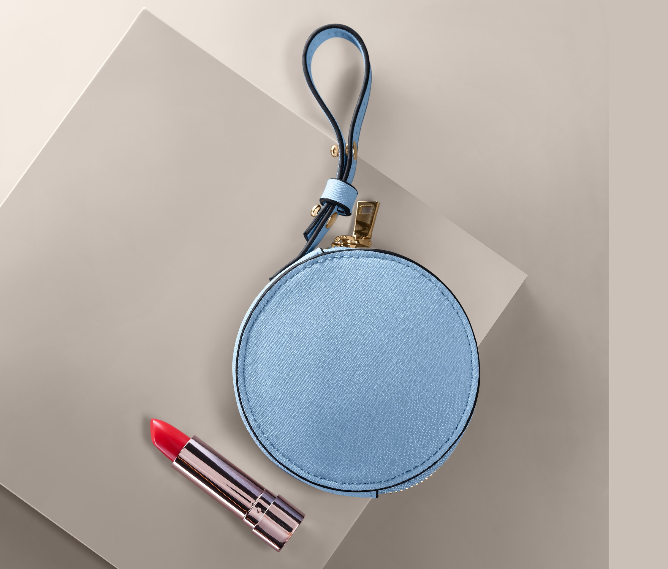 Modrá kulatá peněženka a červená rtěnka na šedém povrchu.