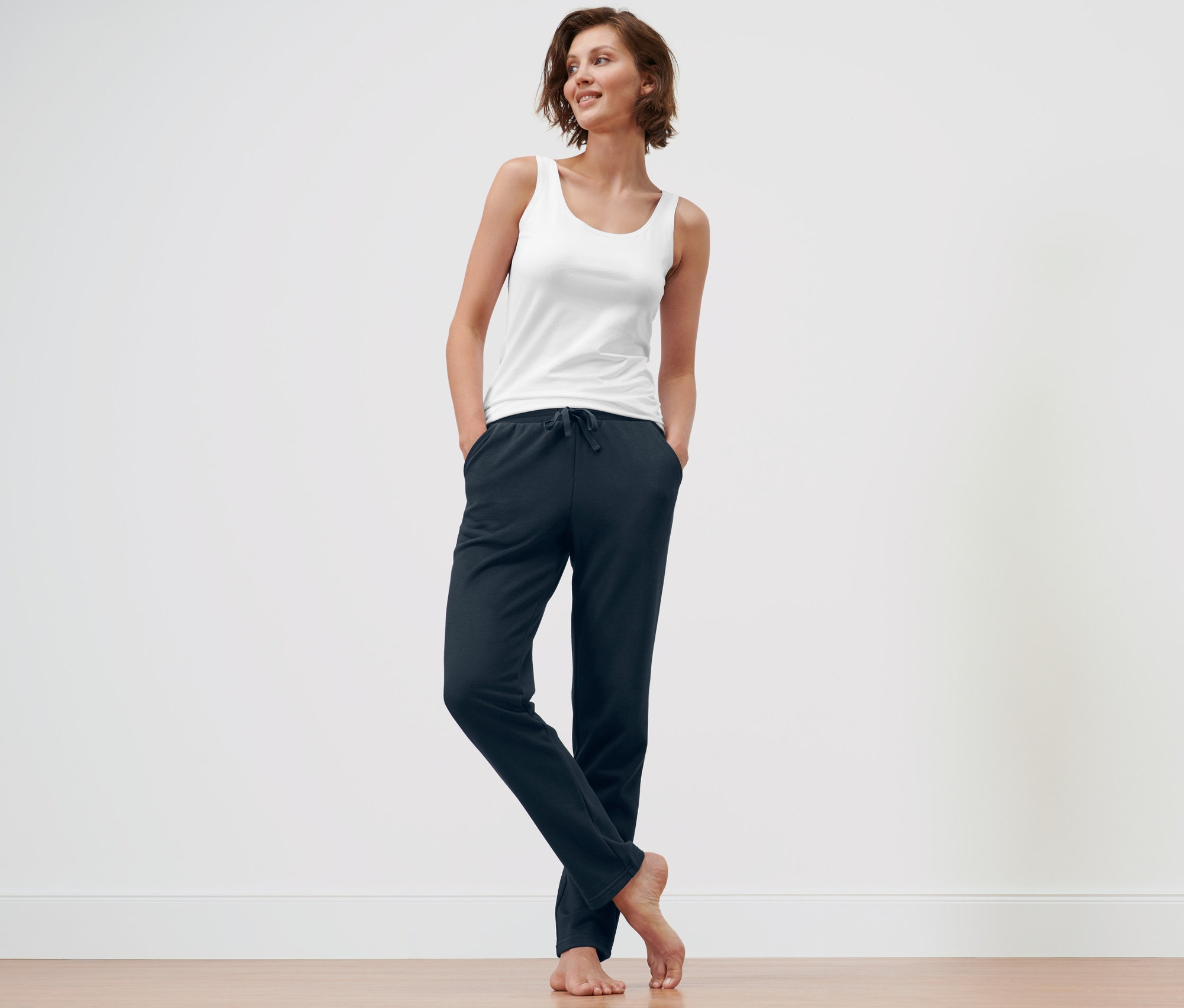 Žena stojí a má ruce v kapsách tmavě modrých pohodlných kalhot a modrých domácích kalhot.