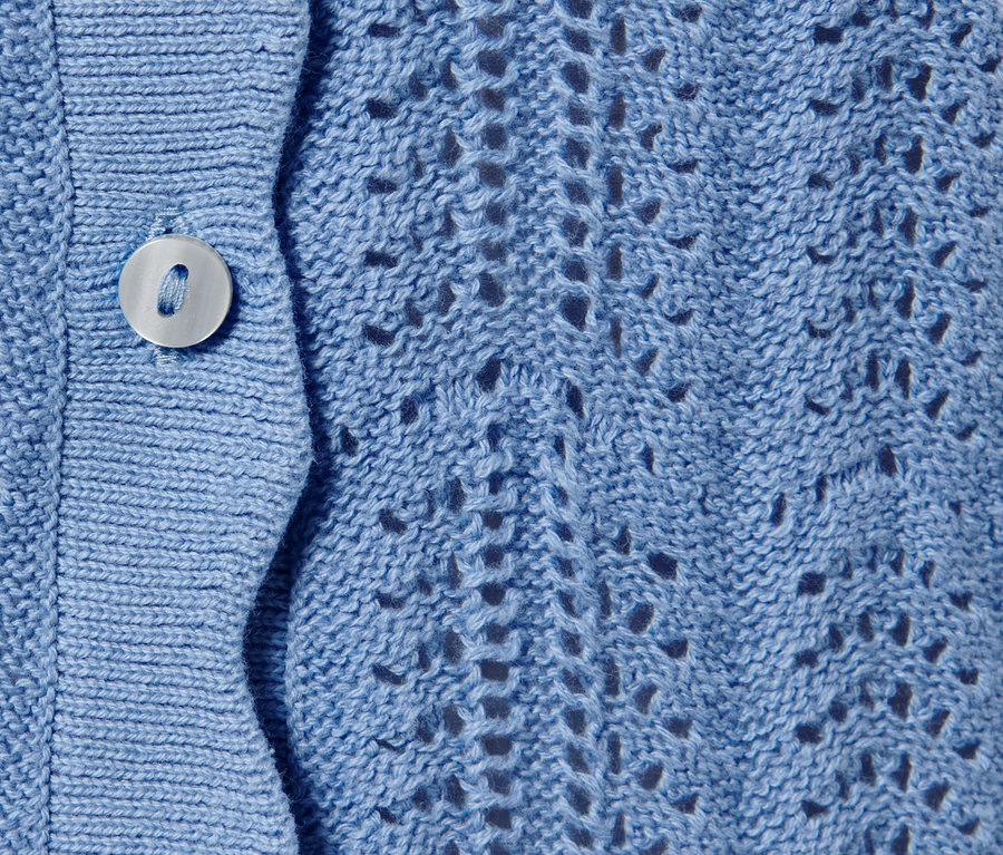 Detail modrého pleteného kabátku s ažurovým vzorem a knoflíkem.