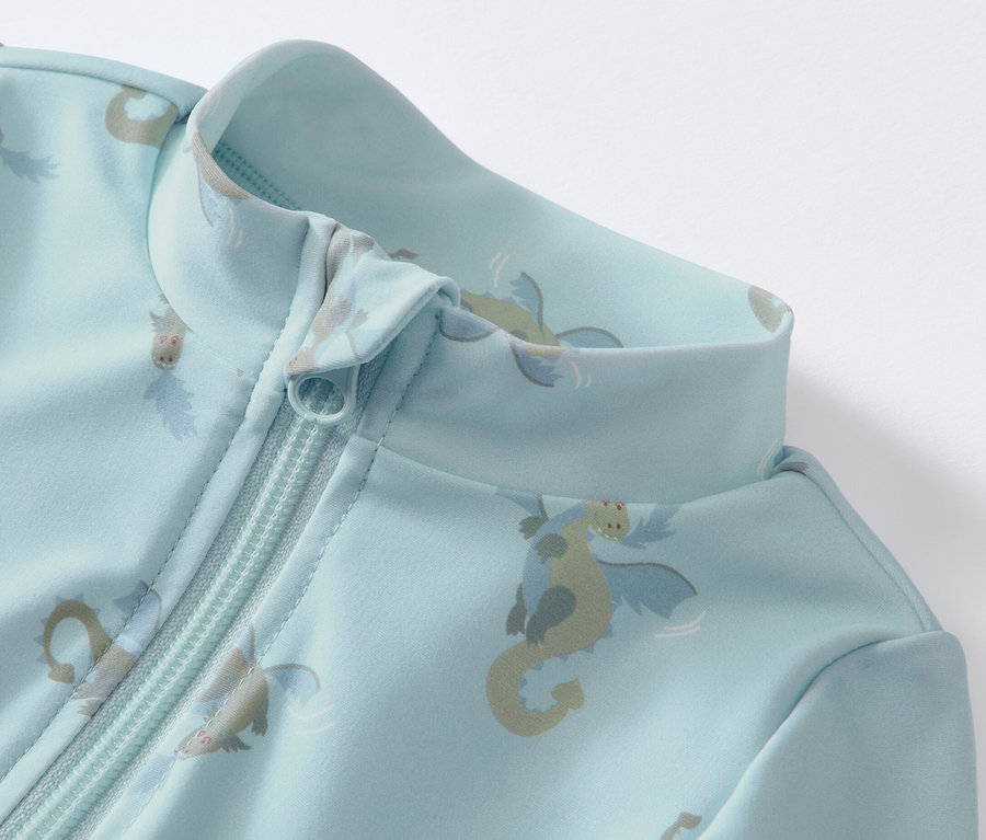 Detail modrého overalu s UV faktorem 80 pro miminka s potiskem dráčků a zipem.