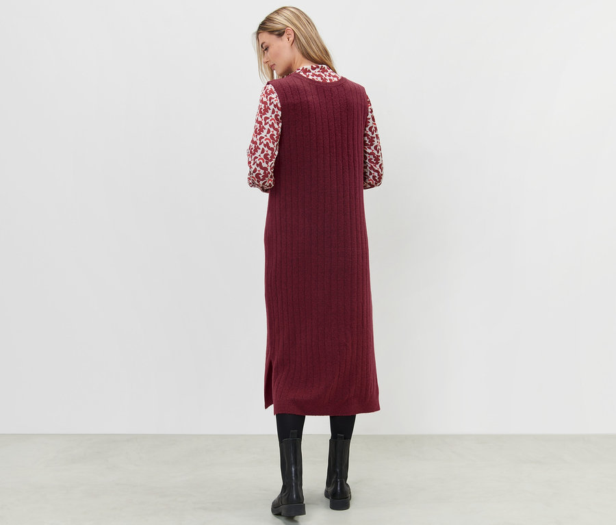 Žena stojí zády a má na sobě červené žebrované pletené šaty.