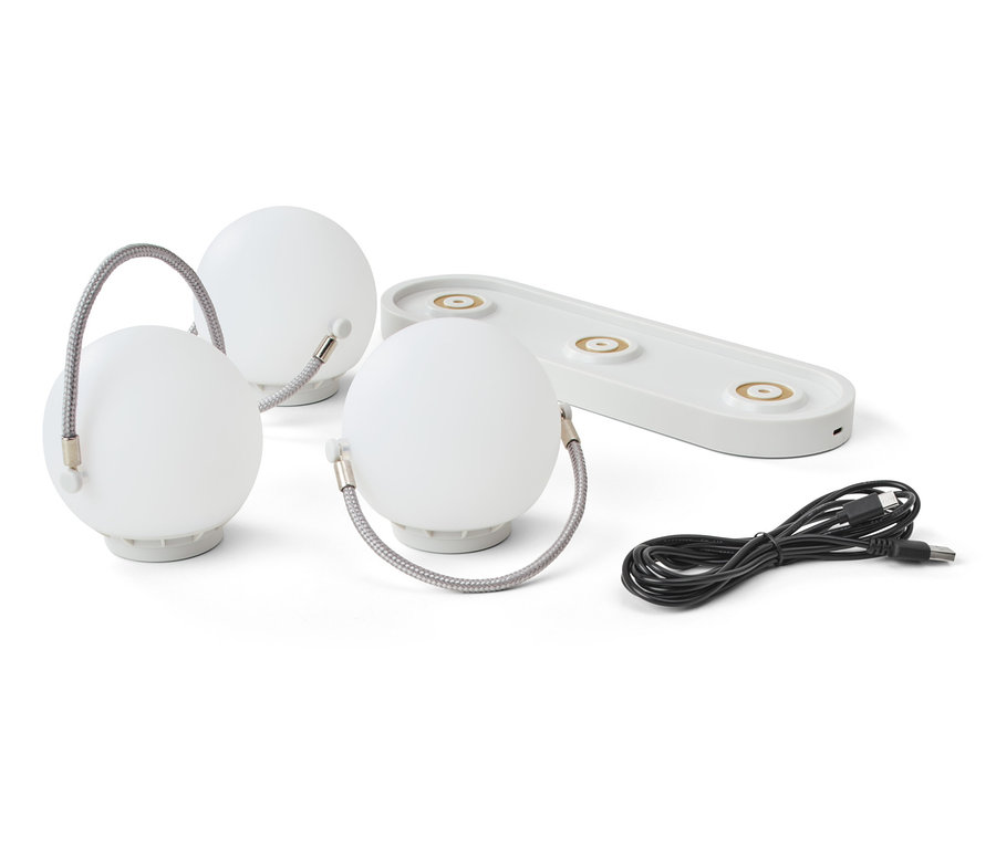 Tři akumulátorové stolní lampy, nabíjecí základna a kabel na bílém pozadí.