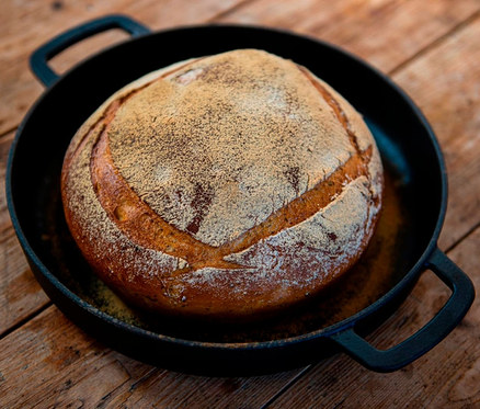 Bochník chleba v litinové servírovací pánvi »COMBEKK Sous-Chef« na dřevěném stole.