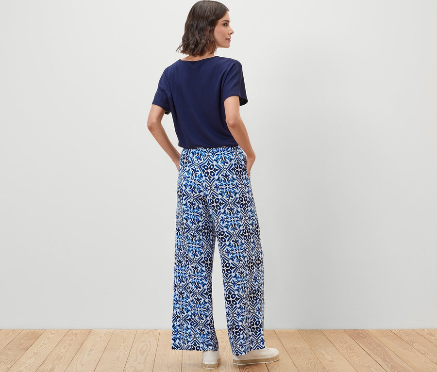 Žena stojí zády a má na sobě modré kalhoty se širokými nohavicemi s potiskem.