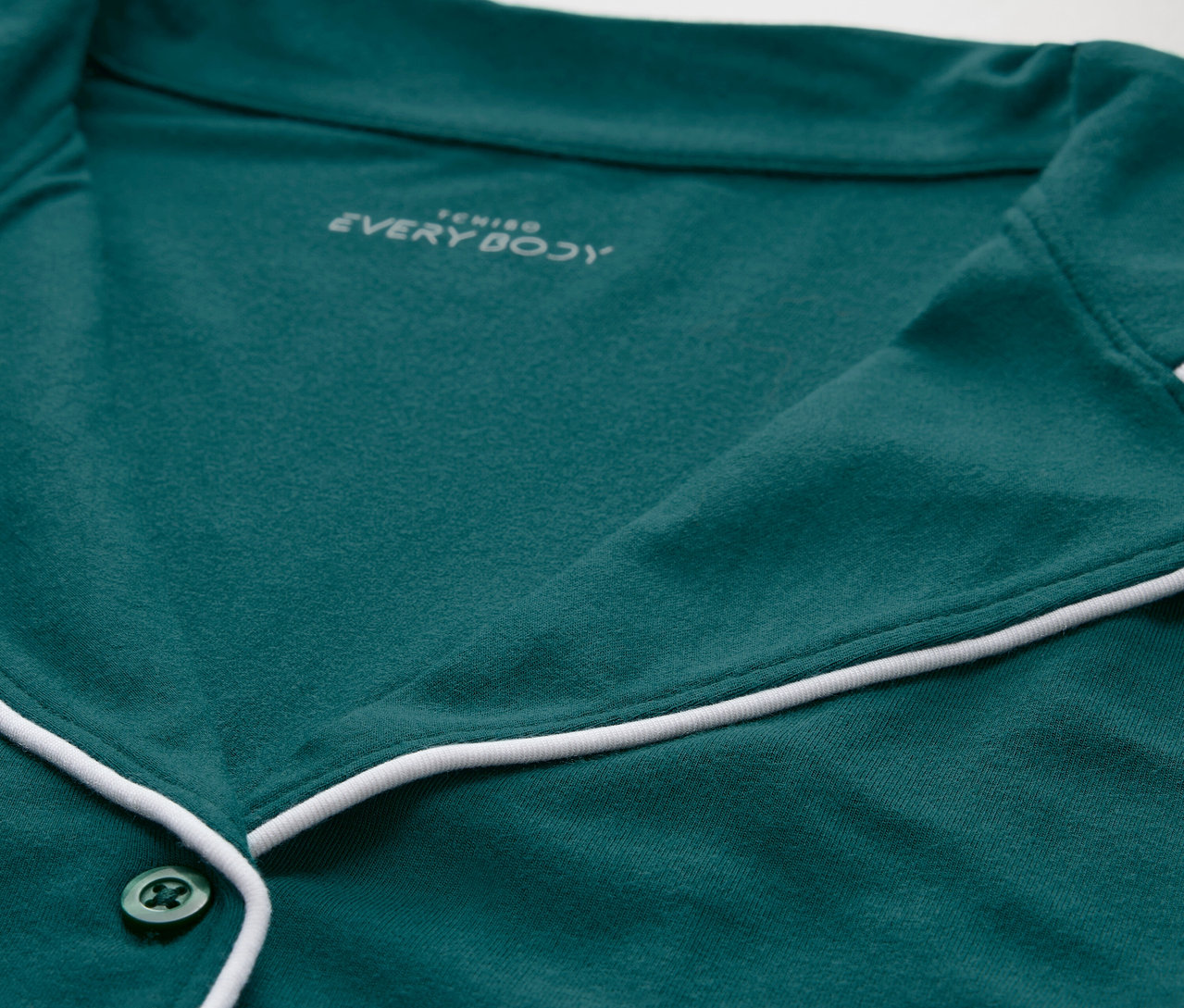 Detail zeleného pyžamového topu s bílým lemováním a knoflíky.