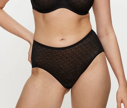Osoba v černých maxi kalhotkách Triumph Signature Sheer Maxi EX z vzorovaného materiálu a sladěné podprsence, s rukama v bocích.