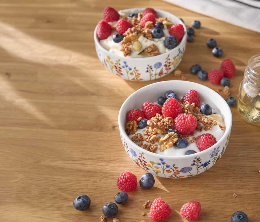 Dvě misky jogurtu s malinami, borůvkami a ořechy na dřevěném stole.