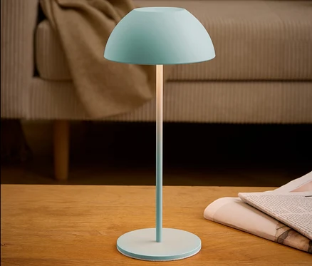 Tyrkysová lampa stojí na stole vedle novin.