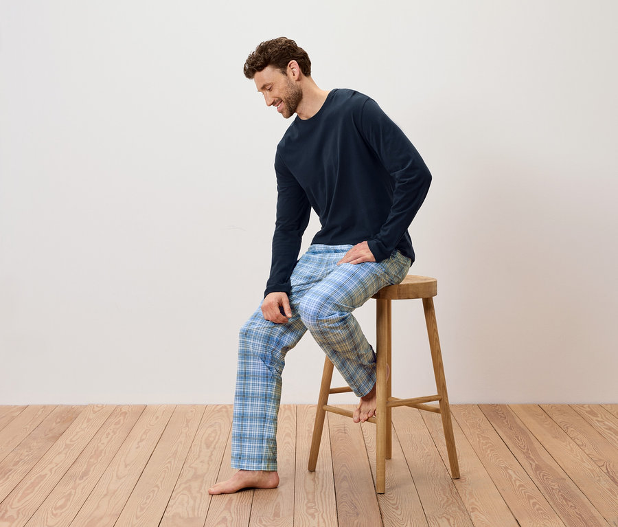 Muž sedí na dřevěné stoličce, má na sobě tmavě modré pyžamo a modré kostkované kalhoty.