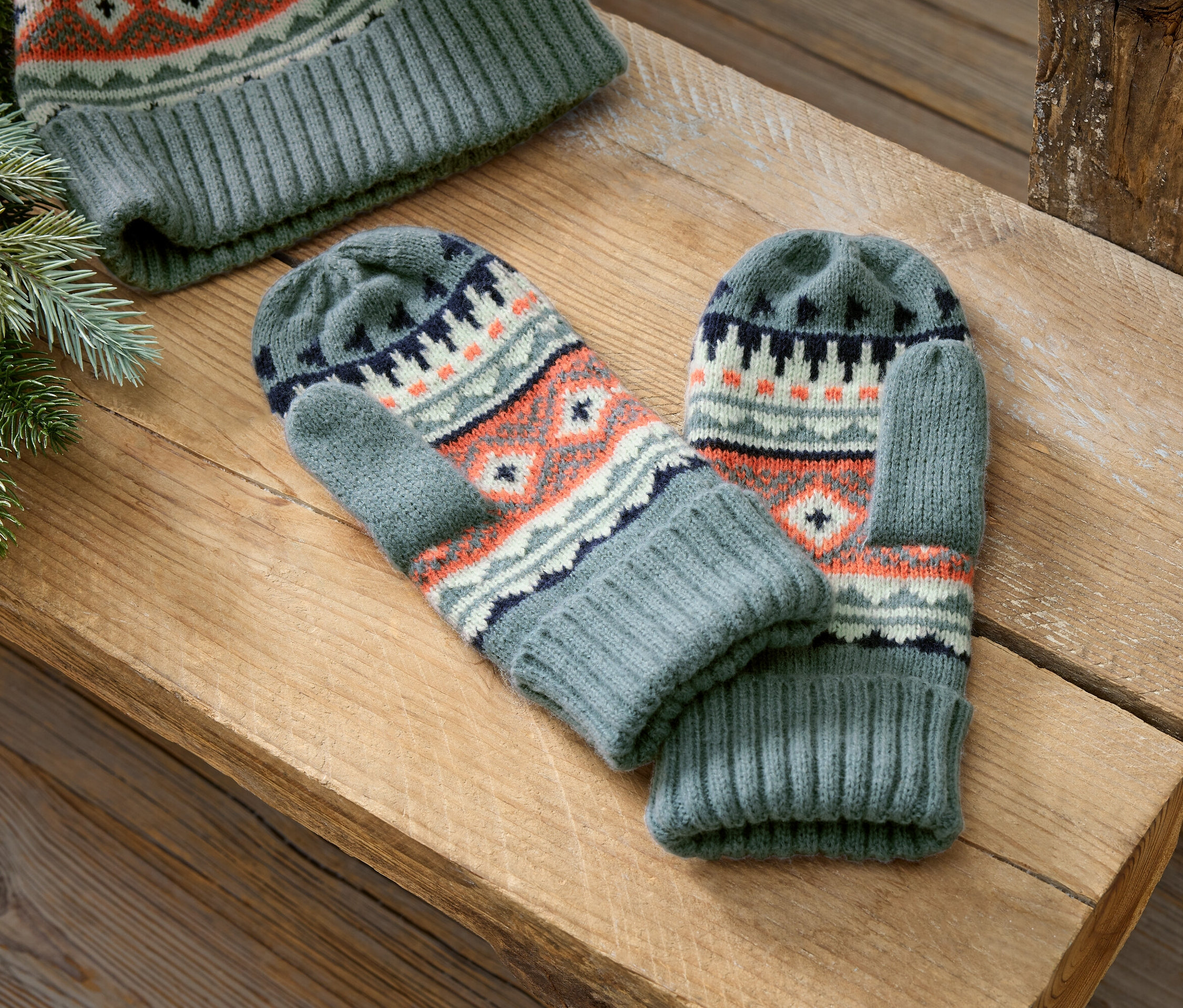 Šedé pletené palčáky a čepice s norským vzorem leží na dřevěném povrchu.