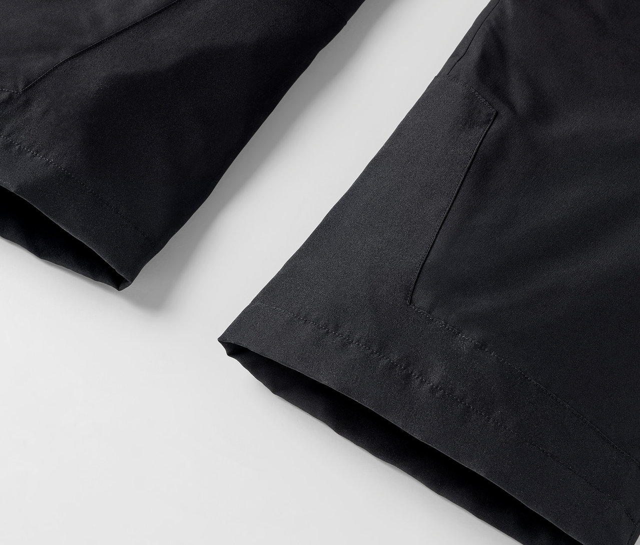 Detail černých kalhot s kapsou na bílém pozadí.