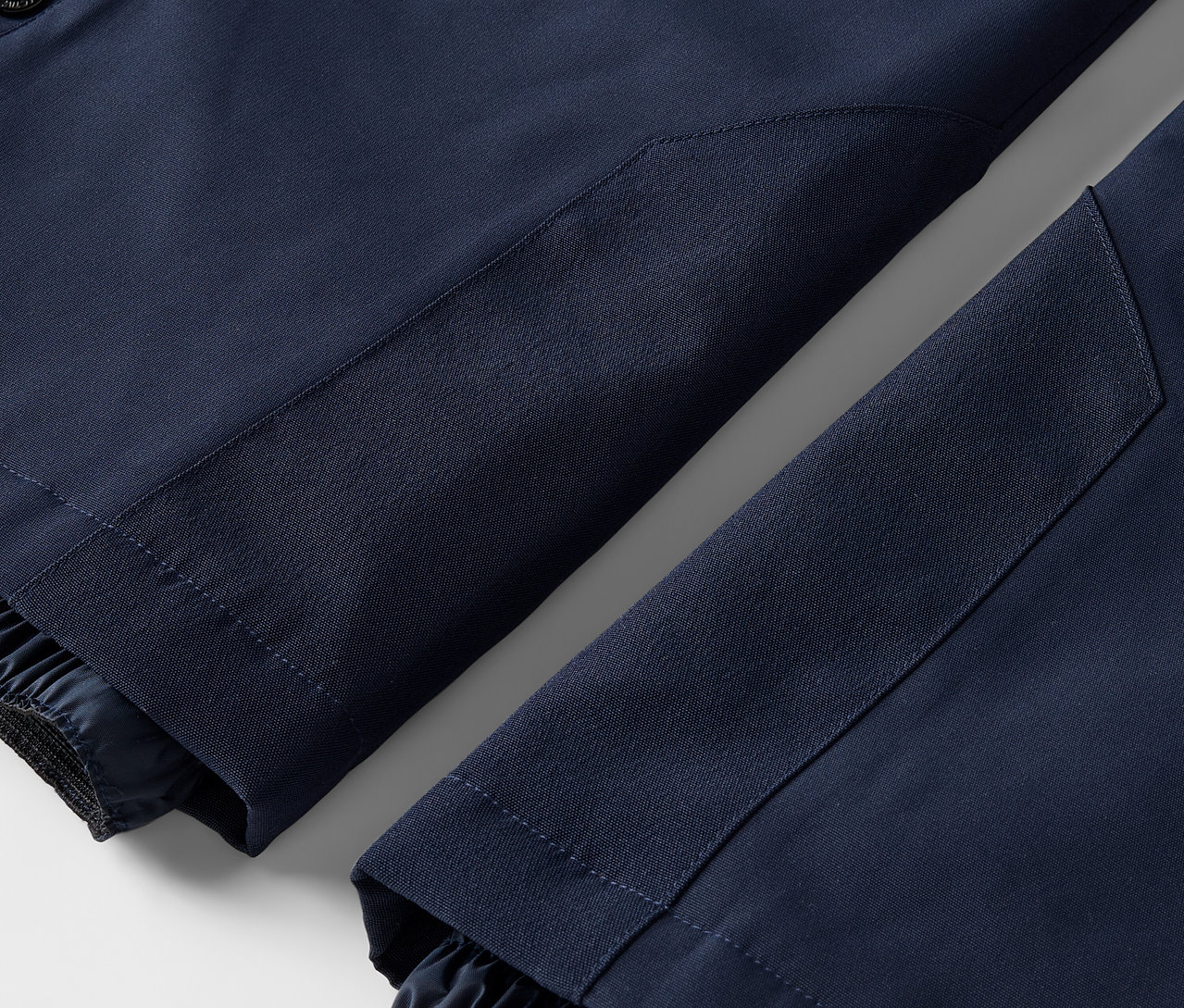 Detail dvou nohavic tmavě modrých kalhot s elastickými lemy.