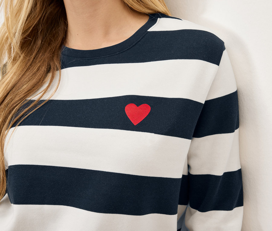 Detail of a woman's torso wearing a striped, long-sleeved shirt with a small red heart on the chest.