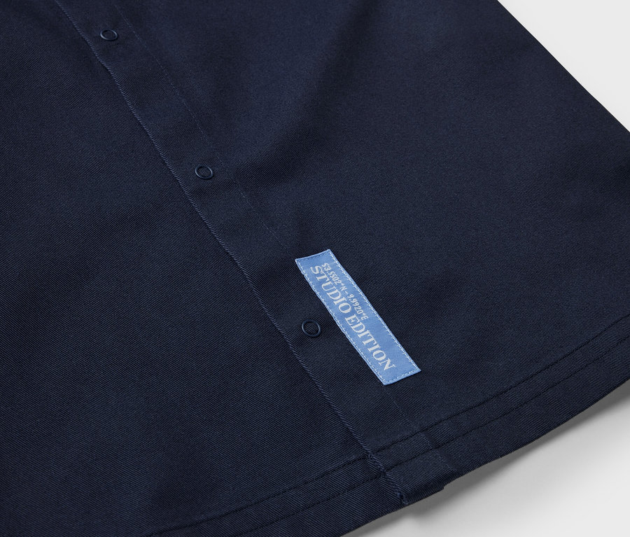 Detail tmavě modré dětské svrchní košile s knoflíky a štítkem Studio Edition.