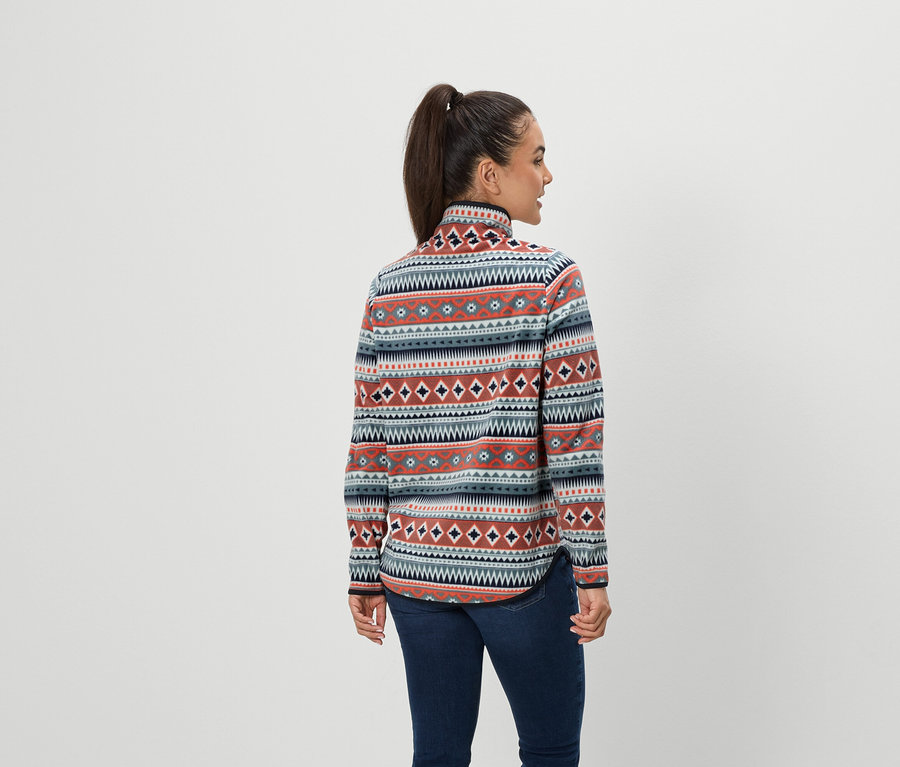 Žena s hnědými vlasy v culíku stojí zády a má na sobě modré džíny a vzorovanou fleecovou mikinu.