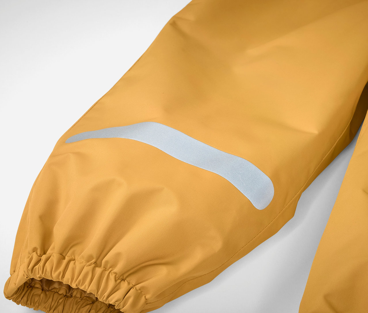 Detail dětských kalhot do deště, žluté barvy, s reflexním pruhem a elastickým lemem.