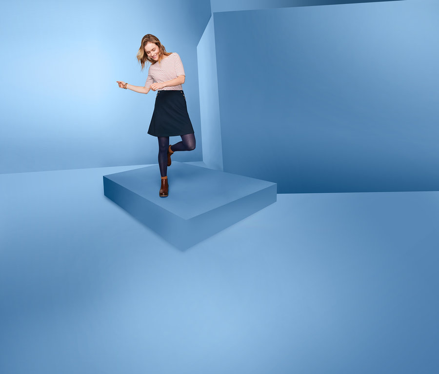 Žena stojí na modré plošině a má na sobě džínovou sukni.