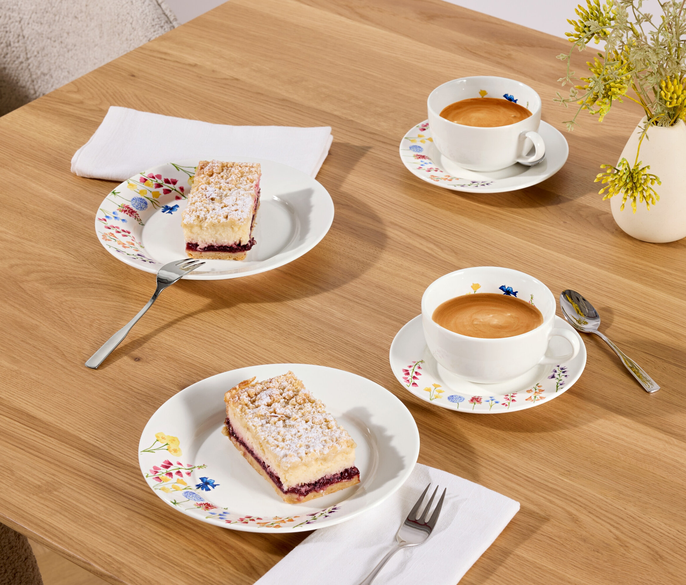 Dva kousky koláče a dva šálky kávy na dřevěném stole.