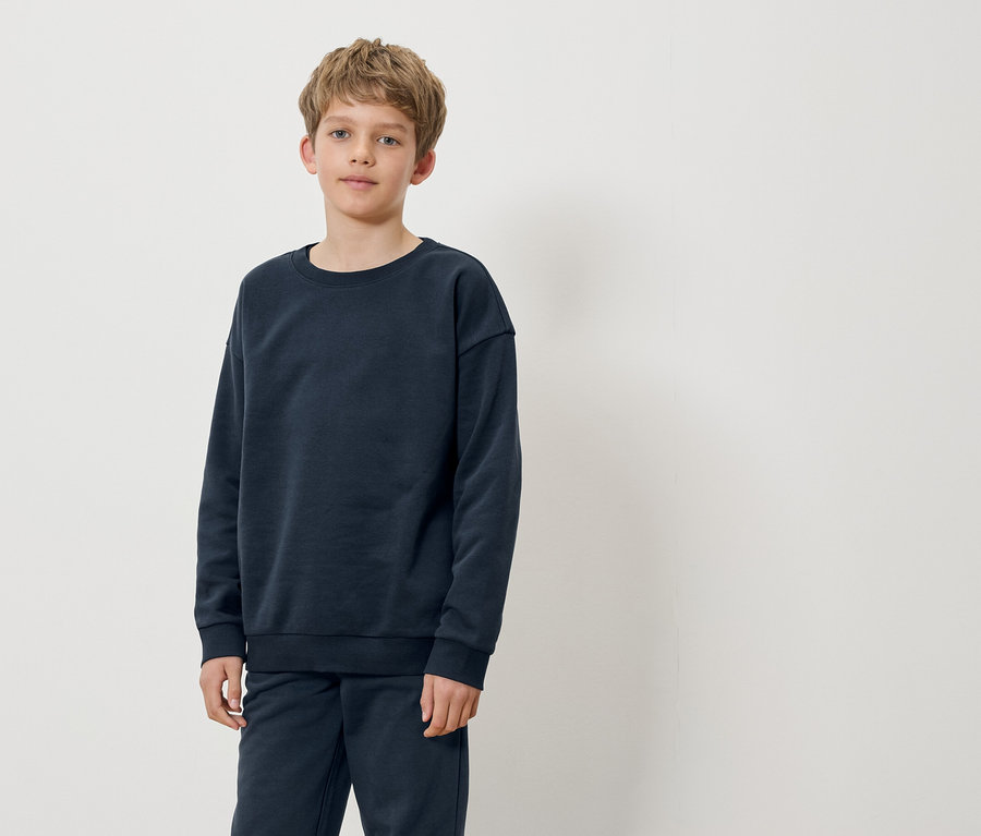 Chlapec stojí a má na sobě tmavě modrou mikinu a kalhoty.