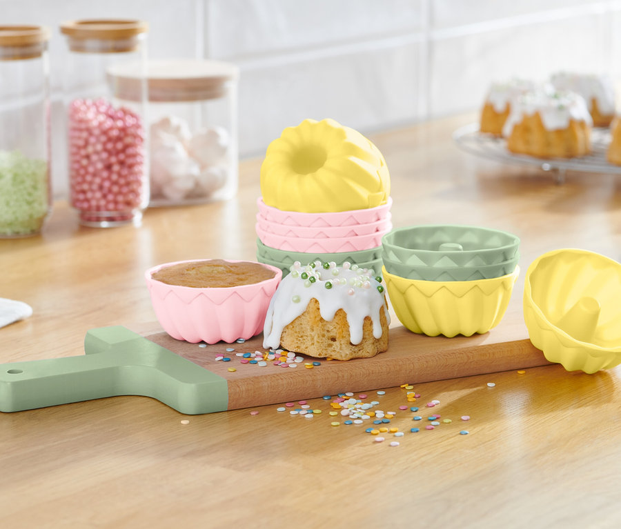 Formičky na bábovky na dřevěném prkénku s hotovými bábovkami a posypem.